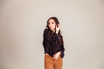 Fototapeta premium beautiful slender young girl with black long hair on a one-ton beige background. woman in brown trousers and black blouse with open back.