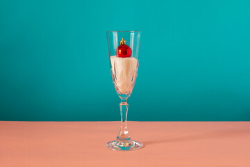 Red ornament inside the glass on pink and blue background. Winter concept.