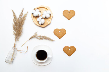 Minimalistic flat lay with pampas grass, cup of coffee and heart shaped gingerbread cookies on white table with place for text.