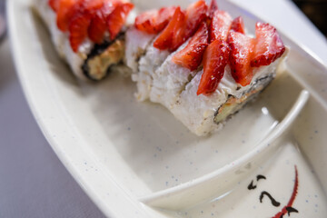 Sushi rolls on a white plate with strawberry slices on top