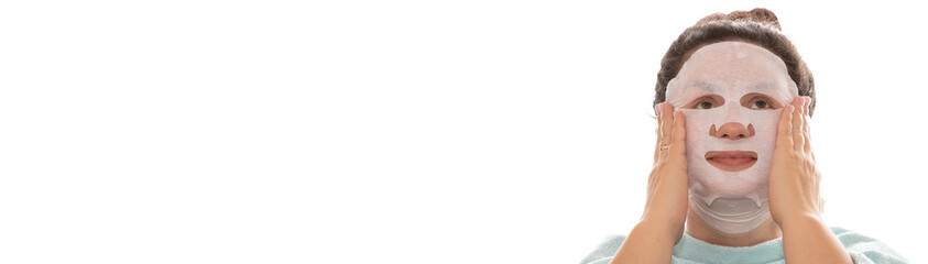 Spa and beauty treatments. Woman with a moisturizing mask on her face touching it with her hands and looking up. Shoulders covered with towel. Isolated on white background. Banner size. Copy space