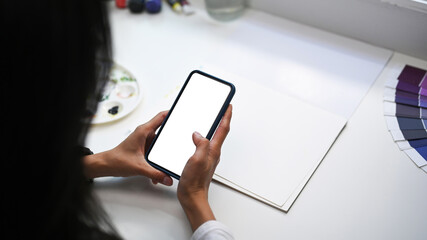 Cropped shot of Artist or designer sitting at creative workspace and using mobile phone.