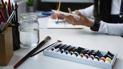 Color tube of water color or oil color and paintbrush on white table with female artist in background.