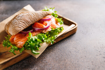 Healthy sandwich with rye bread bun, salmon, avocado, onion and salad served on a wooden rustic board.