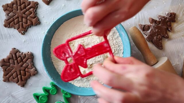 A woman's hand dips a cookie cutter into a bowl of flour, leaving a gift pattern on the surface. Top view, close-up. The concept of cooking Christmas treats