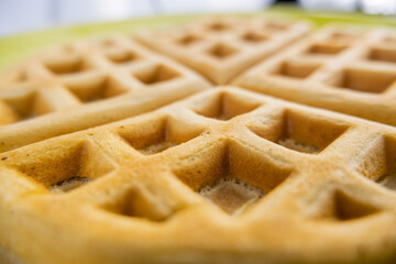 Fresh round waffle on a yellow plate up-close