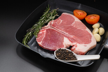 Raw T-bone Steak with fresh herbs and garlic, tomato, black pepper, rosemary on dark black background with copy space for your design, food concept.