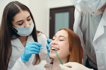 Gloved technicians examine a smiling client's teeth using a dental mirror