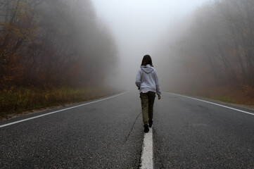 Young woman traveler, rear view on foggy road in autumn forest