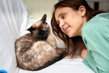 Beautiful woman looking at her cat sitting on a coach at home. concept love of animals.