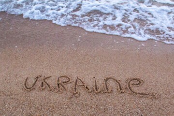 The beach with sea waves running on the sand and the  word UKRAINE is drawn on the sand. Beautiful view on the waves
