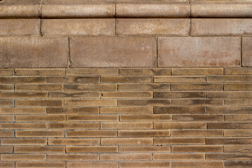 Full frame abstract texture background of a grungy looking vintage light brown brick wall, with narrow bricks in a 1/3 offset pattern, and with larger stone moulding at the top