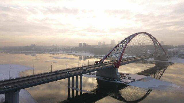 large bridge on the background of sunset is reflected in the river. Cars travel across the bridge in both directions