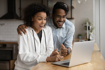 Amazed young biracial couple look at laptop screen shocked by unexpected online sale offer or...