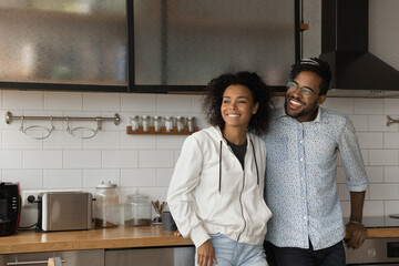 Happy young African American couple renters pose in own modern home look in distance dreaming...