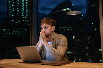 Young Caucasian male employee sit at desk stay in office late hours finish project or research on...