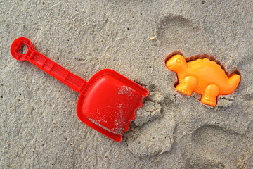 Summer concept on the sandy beach, a spade and a dinosaur sand mold on the beach