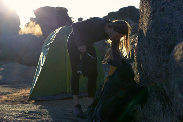 Woman unpacks her backpack outside of her tent at dawn