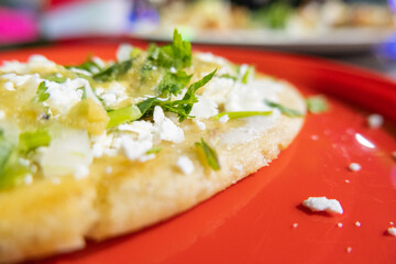 Tlacoyo with cheese, green sauce, and sour cream on a red plate