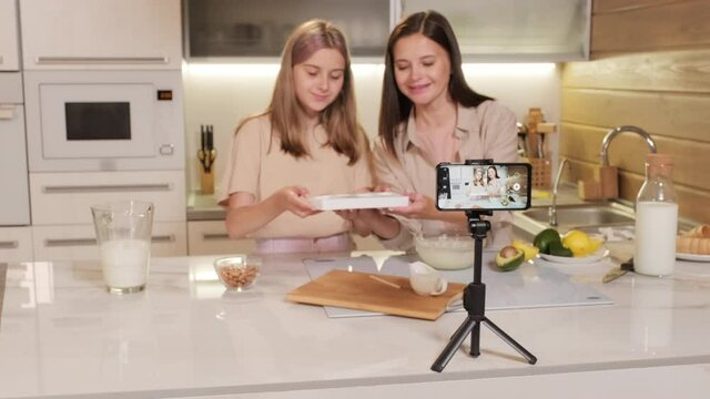 Waist-up Footage Of Joyful Energetic Mom And Daughter Filming Video Of Making Natural Ice-cream At Home Pouring Mixture Into Silicon Forms Showing Result To Phone Camera On Tripod