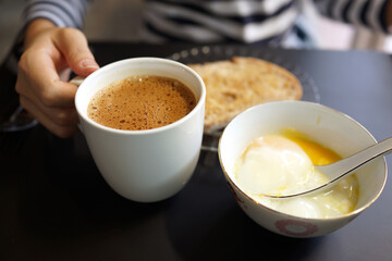 Coffee to go. Close up female hand holding a cup of latte and enjoying breakfast in a cafe.