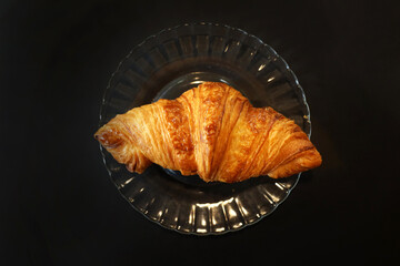 Fresh croissant on a plate, black background