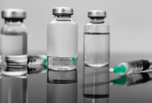 Medical treatment syringes and vaccine bottles in reflecting dark table