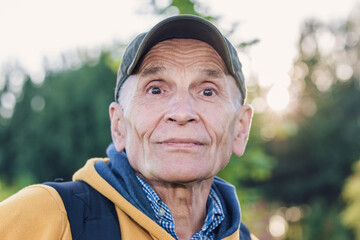 Head outdoor portrait of aged man in green cap and with backpack.