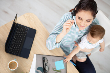 mother holding baby while working on laptop in office