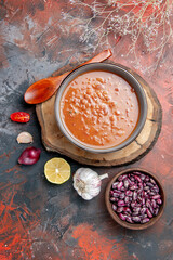 Side view of classic tomato soup in a blue bowl on wooden tray oil bottle beans garlic onion tomato on mixed color background