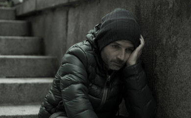 dark and edgy urban portrait of middle aged sad and depressed unemployed man sitting outdoors on dirty street corner staircase feeling upset suffering depression problem