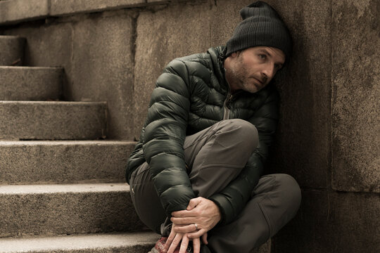 dark and edgy urban portrait of middle aged sad and depressed unemployed man sitting outdoors on dirty street corner staircase feeling upset suffering depression problem