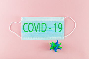 Therapeutic  surgical mask for protection against flu and other viral diseases, with a model of a coronavirus bacterium made of plasticine. Protective mask on a pink paper background against the sprea