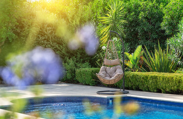 Luxurious pool in the garden of a private villa, hanging chair with pillows for leisure tourists,...