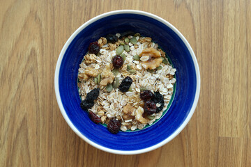 A bowl of cereal oat granola, walnuts and raisins on wooden background. Healthy vegan food.