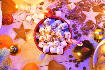 Fototapeta premium sweet food top view background for merry christmas or new year holiday decoration with night illumination - chocolate candies, tangerines, cookies, marshmallow and cocoa latte on white wood