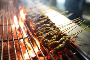 Chicken satay grilled on grills plate with smoke.