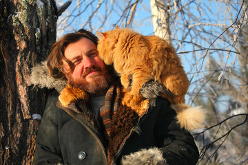 a bearded man with a red cat on the background of a winter forest