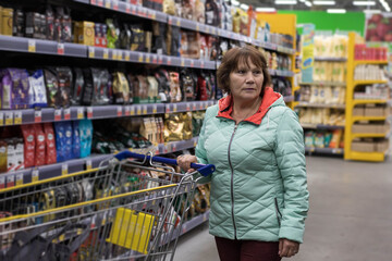 A woman with a shopping trolley looks at some products in the aisle of a supermarket.