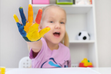 Beautiful blond toddler girl with colorful painted on her hands