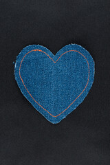 Denim heart with orange threads lies on black silk.