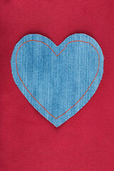 Denim heart with orange threads lies on red silk.