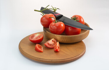 Tomatoes and a knife in a wooden plate and slices on a round wooden tray on a light background.