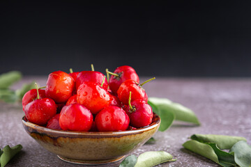 Ripe red cherries in a ceramic bowl with sunlight on the black wall background. Space for text. Sweet organic berries. Concept of healthy fruits