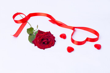 Fototapeta na wymiar Red rose, ribbon and hearts on a white background. Valentine's Day, Birthday, Mother's Day, International Women's Day. Close-up, selective focus.