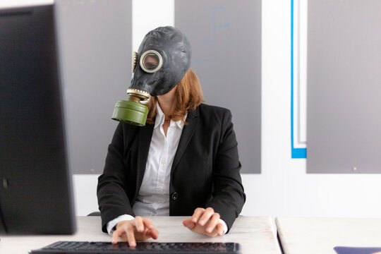 woman working on a computer in the office, business woman in a suit with gas mask because of corona, virus free office woman wearing a soviet gas helmet; 
decontamination staff in office; hacker
