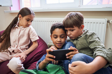 Three multiracial pupils sitting at the soft poufs