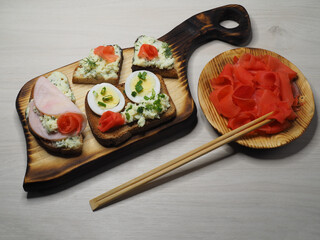 Sandwiches, bruschetta, cheese toast, ham, spicy herbs, egg and pickled ginger on a wooden Board, light background, top view. Fast food recipe, snack with fried bread for a holiday and picnic