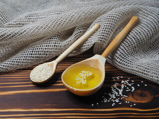 Sesame in a wooden spoon and sesame oil in a wooden spoon on a wooden background with a napkin,...