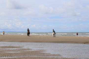 Fototapeta na wymiar Two girls riding horses on the beach at Ynyslas, Ceredigion, Wales, UK. 